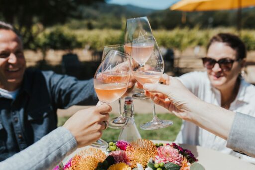 Hand with glasses of pink sparkling wine raised in a toast with vineyards in the background