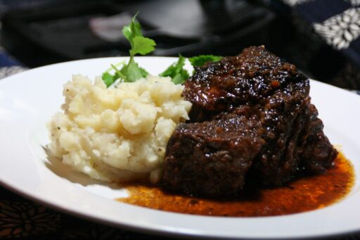 mashed potatoes, braised beef with sauc and parsley on a white dinner plate