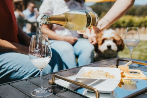 A bottle of Amista white wine being poured into a wine glass with the Amista logo, sitting on a wood table with wine pairings.