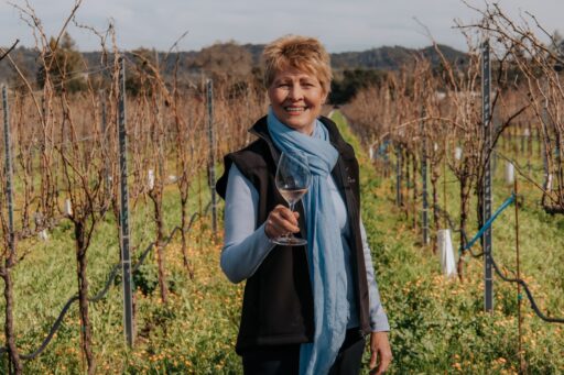 Amista Proprietor Vicky Farrow standing in vineyard holding a glass of sparkling wine