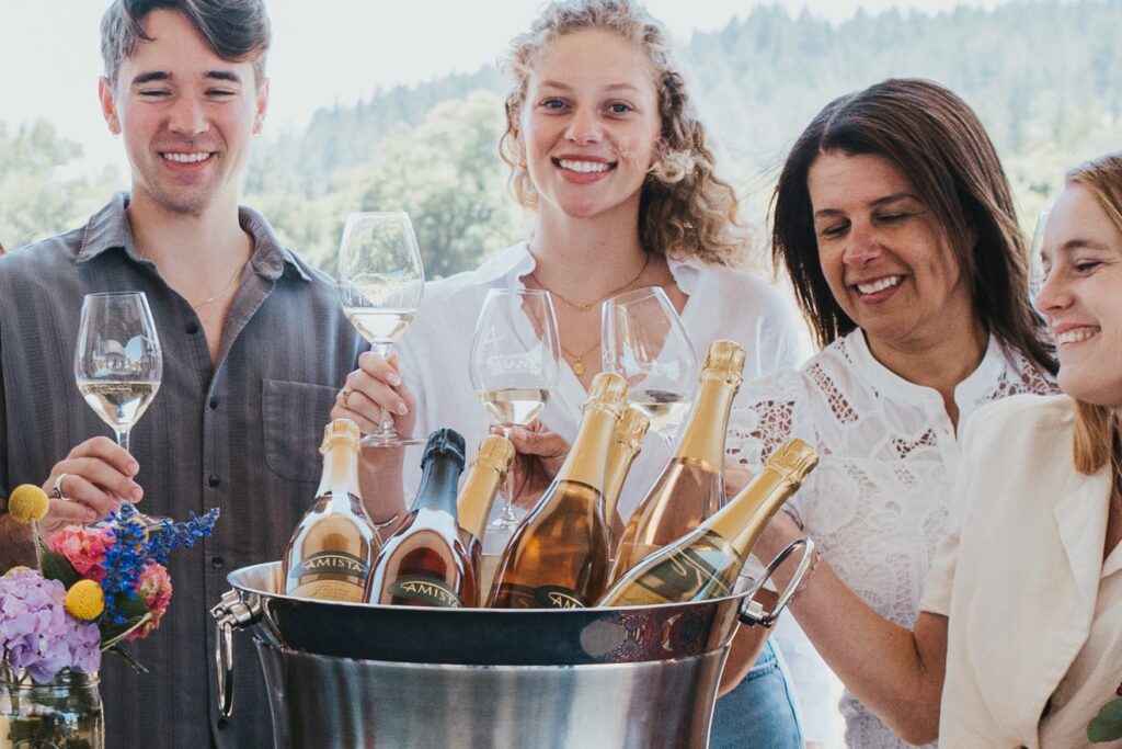 Smiling man and three women holding wine glasses behind a bucket of Amisra spakling wines