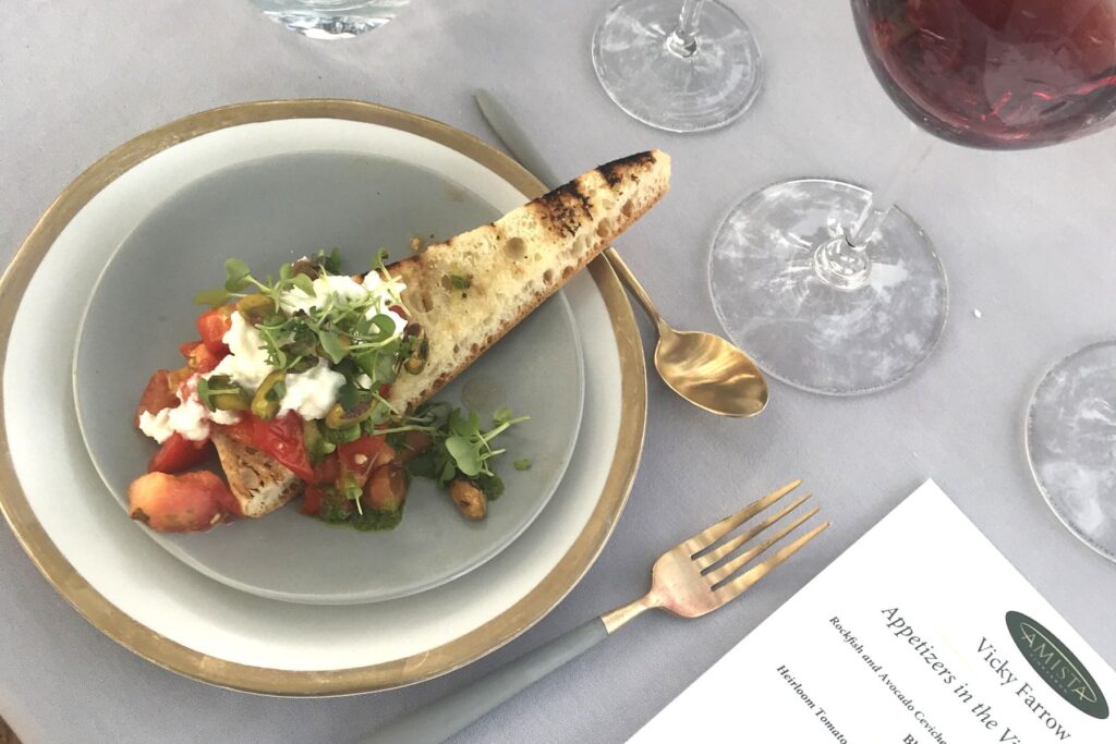 Tomato and burrata bruchetta on a plate with wine glasses at Amista Dinner in the Vineyard