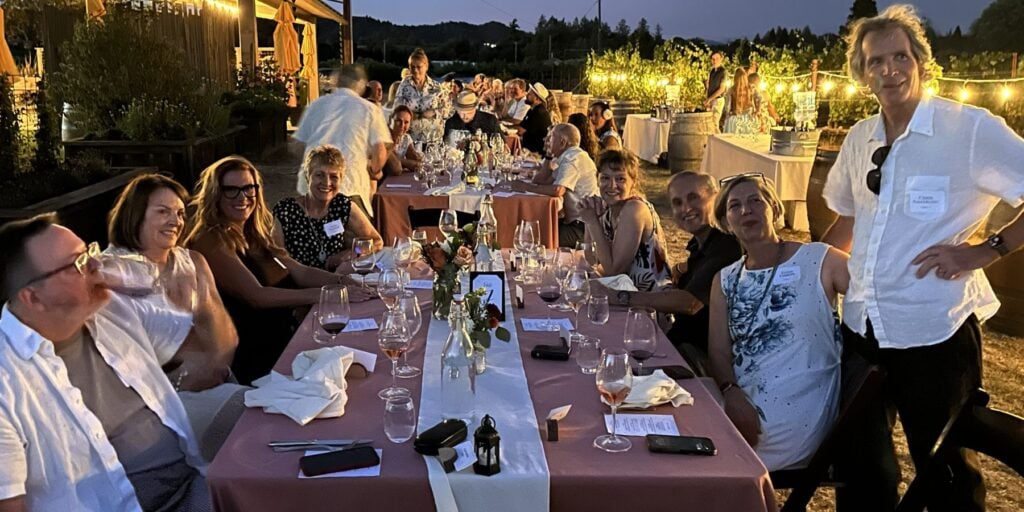 Guests around a table in a vineyard with twinkling lights at Amista Dinner in the Vineyard